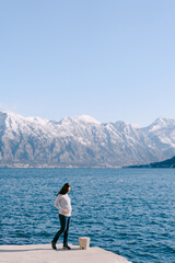 Pregnant woman stands on a pier against the backdrop of mountains and sea