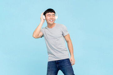 Portrait of happy smiling young Asian man with wireless headphones listening to music on isolated ...