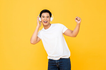 Young handsome Asian man with headphonesdancing and listening to music on studio yellow background