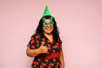 Body positive fat latin adult woman with christmas hat and glasses shows her enthusiasm for the arrival of december and celebrating christmas
