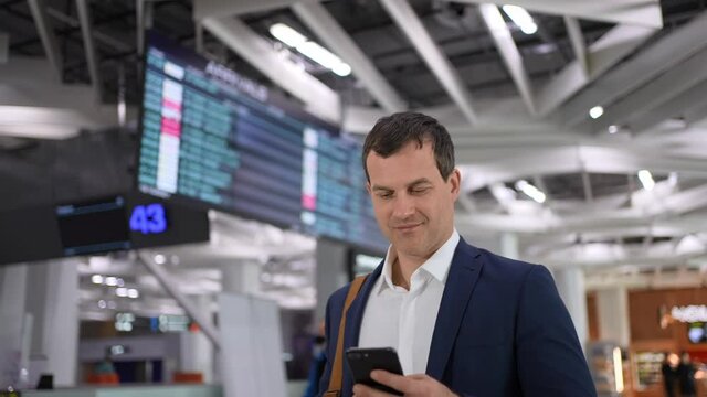 Tourist traveler man using mobile phone of plane arrivals board in airport terminal for trip travel. Businessman typing text message on smartphon for check-in at flight, Technologies business concept