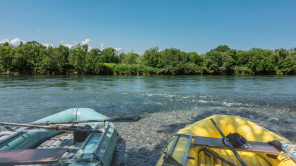 Two colorful inflatable boats are standing on the river bank. The pebbles on the bottom are...