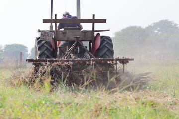 An Indian male laborer farmer plowing the field with the help of a tractor plow