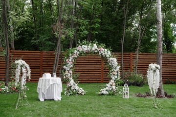 Circle wedding arch decorated with white, pink flowers and greenery outdoors, copy space. Wedding setting on back yard. Floral composition