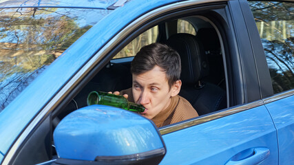 Driver brunet short-haired man sits in car cabin and drinks alcohol from glass bottle secretly...