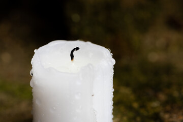 An extinguished candle after the rain. Black wick and drops of water on the wax. Front view.