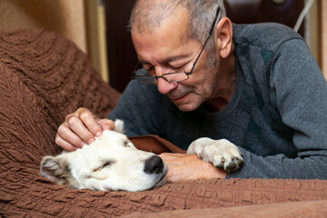 Male owner cuddling his white dog sleeping on the couch. Close-up portrait.