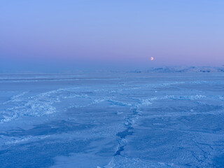 Moon over frozen Disko Bay during winter, West Greenland, Disko Island in the background....