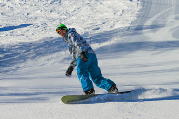 A handsome young man slides down a ski slope on a snowboard. Snow flies out from under his board. A...
