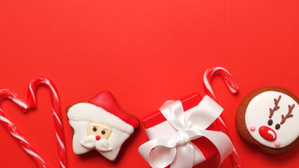 Christmas background with santa claus gingerbread man cookies with red gift box on a red background, flat lay with copy space