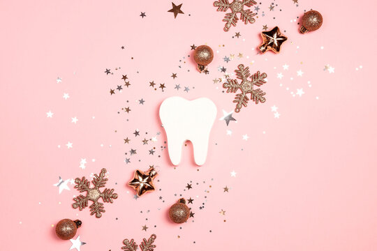 White tooth with gold decorations on pink background. Dentist Merry Christmas and New Year concept.