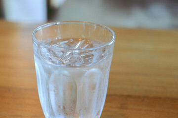 Glass of cold water with some ice on wooden table.