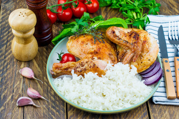 a plate of grilled fried chicken and boiled rice. tomatoes, cockerel greens, garlic on a wooden board. rustic wooden background.