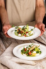 Female hands are holding an gourmet fish salad. Pangasius dori fillet, vegetables, avocado pate, mozzarella and fresh herbs. Restaurant serving. Chef's dish. Healthy and tasty food. Fish dishes