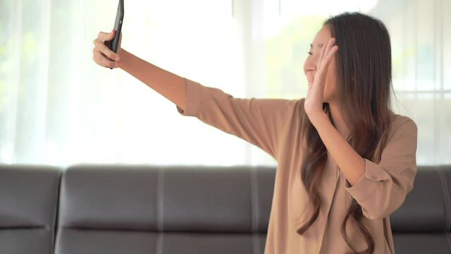 A pretty young woman on a facetime call smiles, and waves to the person on the other end.