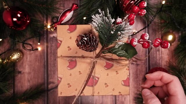 Unboxing a Christmas gift box. Untying the twine. Wooden background with fir branches, red balls, toys for the Christmas tree. The garland glows with warm light. POV. Top View 4K