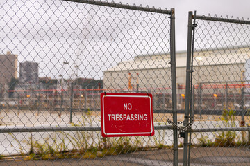 No trespassing sing hanged on an wire fence in front of a dockyard. It says that passing from here is forbidden.