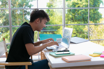 Attractive happy young man student studying at the college library and sitting at the desk using laptop computer, having video chat.