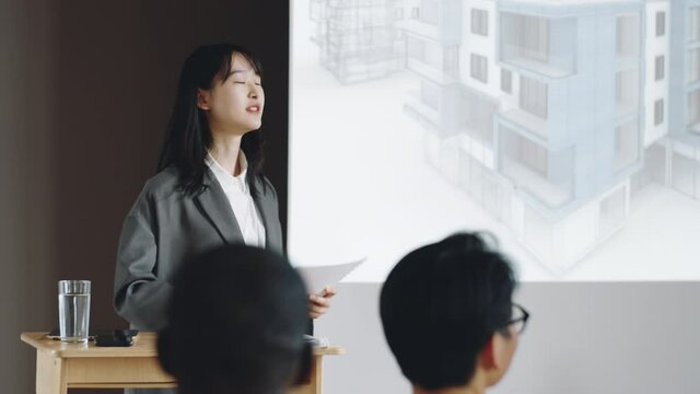 Young Asian woman smiling and giving presentation to colleagues during architecture conference