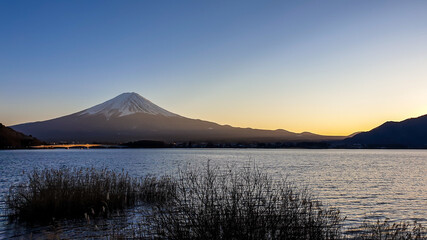 Idyllic view on Mt Fuji from the side of Kawaguchiko Lake, Japan. The mountain is surrounded by clouds. Calm surface of the lake moved by gentle wind. Serenity and calmness. Soft colors of the sunset