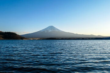 A close up view on Mt Fuji from the side of Kawaguchiko Lake, Japan. Soft colors of sunset - golden hour. Top of the volcano covered with a snow layer. Serenity and calmness. Calm lake's surface