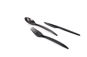 A set of plastic cutlery knife, fork and spoon in black, filmed on a white background