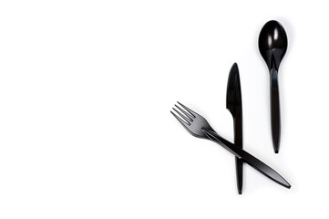 A set of plastic cutlery knife, fork and spoon in black, filmed on a white background