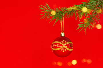 close up of a beautiful red christmas bauble hanging on a fir branch against a red background with copy space