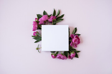 Flowers composition. Wreath made of pink peonies flowers, blank square paper sheet on pink...