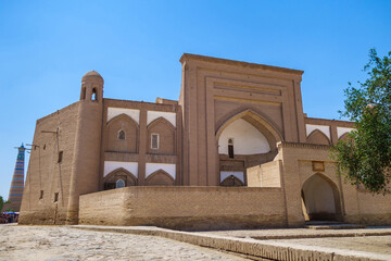 Fototapeta na wymiar Madrasah of Arab Muhammad Khan, one of the oldest buildings in Khiva, Uzbekistan. Built in 1616. Silhouette of the famous Islam Khoja minaret is visible in the distance
