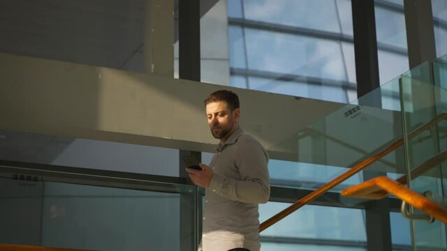 Slow motion of businessman walking down the stairs in the office building looking at mobile phone browsing online sunset sunshine on his face idea come into his mind get inspired 