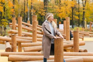 Young beautiful woman in stylish casual outfit standing on the wooden logs on playground