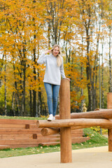Naklejka na ściany i meble Young beautiful woman in stylish casual outfit standing on the wooden logs on playground