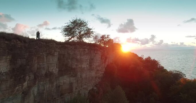 Aerial view of young couple huggin on cliff edge on sunset.