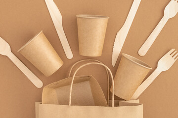 Zero waste, plastic free concept. Paper bag with disposable paper cups, plate, wooden forks and knives on beige background. Eco sustainable living