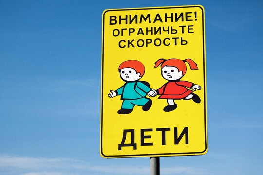 Road warning sign near school or kindergarten. Translation of inscription: "Attention! Limit the speed - children" (in Russian)