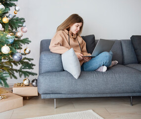 Teenage girl with laptop sitting on sofa in living room