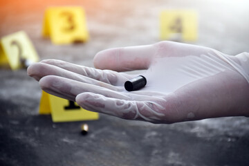 Forensic officer is holding handgun casings or pistol bullet which is important physical evidence while collecting evidence at the scene of the crime. Soft and selective focus.