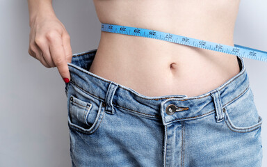 Woman in jeans measuring her waist, isolated on white background
