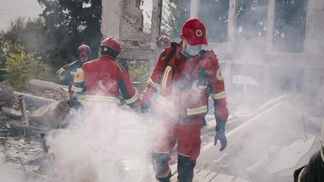 Male paramedic in mask walking on remains of destructed building near colleagues during rescue mission after cataclysm