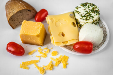 Various types of cheese, tomato and bread on white table.