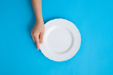 woman holding empty plate with one hand on blue background