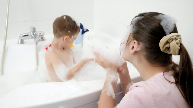 Funny mother with son splashing water in bath and throwing soap suds. Concept of hygine, children development and fun at home