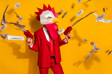 Photo of funky authentic guy hold money gun shoot cash wear rooster mask red suit isolated yellow...