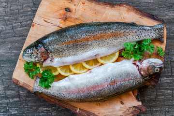 Two fresh raw rainbow trouts garnished with lemon slices and parsely