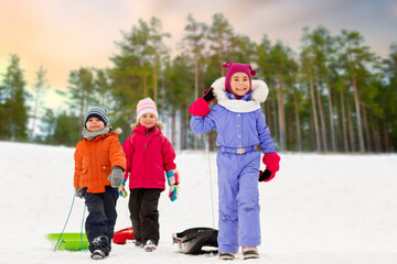 childhood, sledging and season concept - group of happy little children with sleds in winter over...