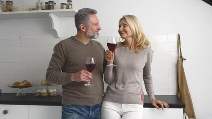 Lovely middle-aged couple has romantic evening, grey-haired handsome man hugging beautiful blonde woman, mature spouses enjoying time together at home, drinking wine and laughing, flirting