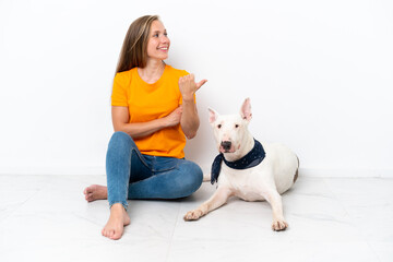 Obraz premium Young English woman sitting on the floor with her dog isolated on white background pointing to the side to present a product