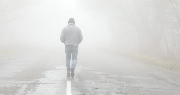 Fog landscape. Man walking  alone on scary foggy misty road. 