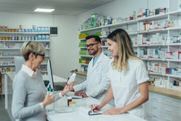 Male pharmacist working on a computer while female pharmacist is giving prescription medications to senior patient